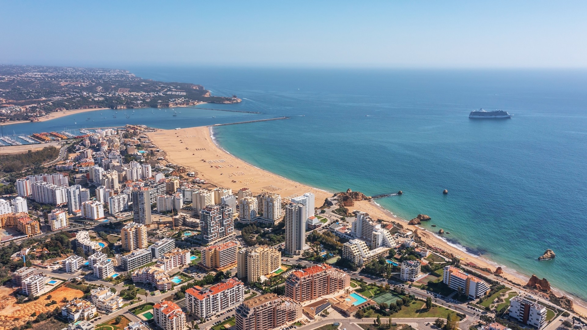 Aerial view of the Portuguese city of Portimao with high-rise buildings on the coast with beaches. Tourist cruise liner in the background in the sea.